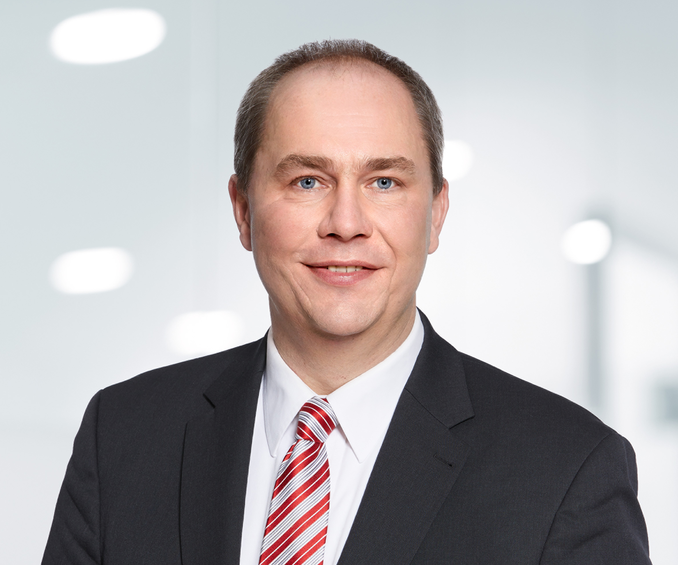 Portrait photo of friendly smiling man in black jacket with short hair and red striped tie