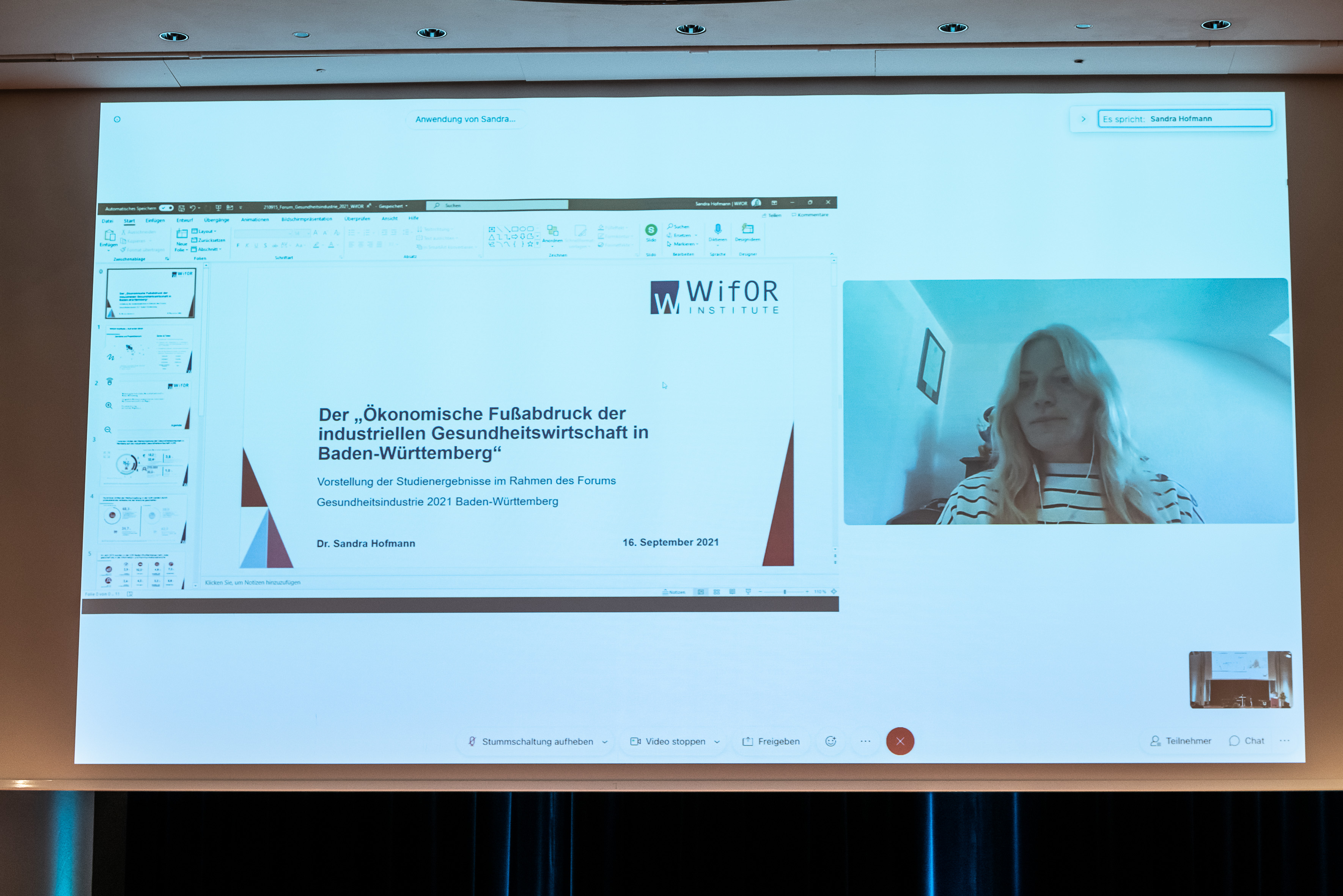 Präsentationsfolien auf einer Leinwand und eine Person die virtuell daran teilnimmt