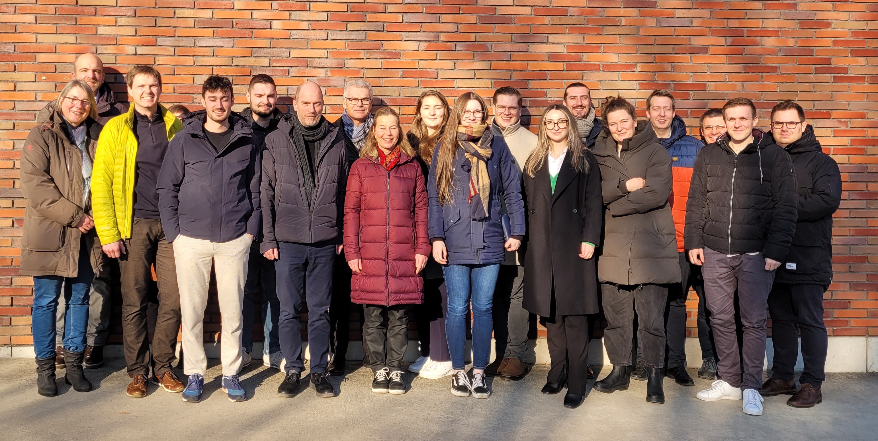 Vor einer roten Backsteinwand stehen 19 Personen – Vertreterinnen und Vertreter aus dem Projektkonsortium.