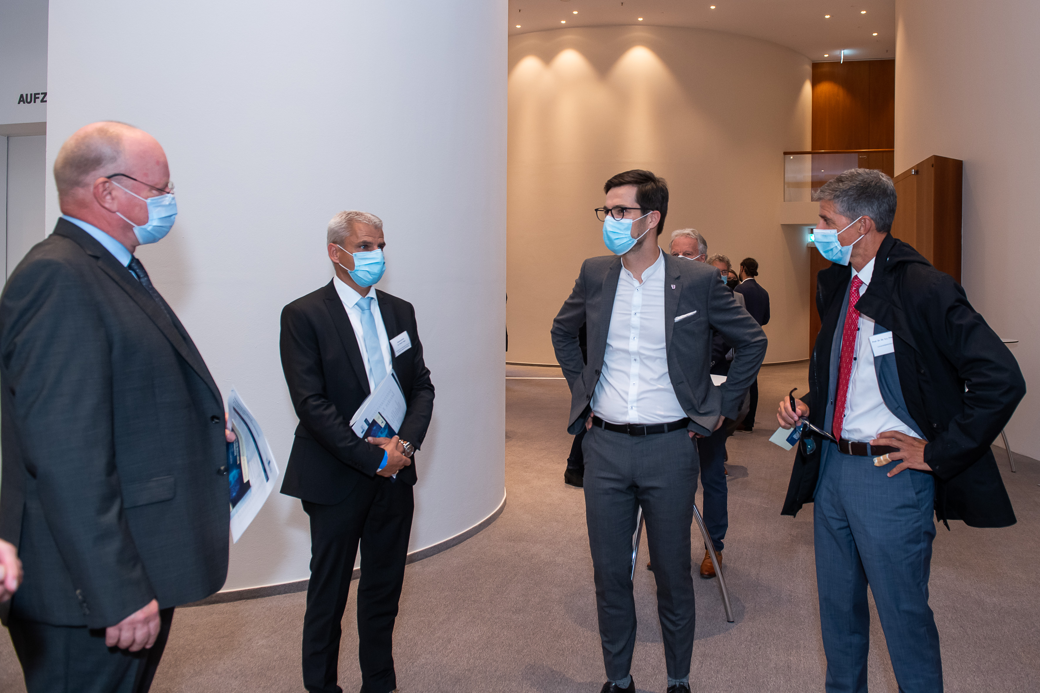 Ein Bild von Leuten in einem Raum, die eine Corona Maske tragen.