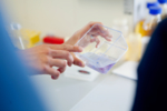 The photo shows the hands of a scientist rotating a flask with a red liquid.