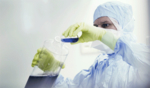 Ein Mann in Laborkleidung füllt blaue Flüssigkeit aus einem kleinen Behälter in einen großen Behälter.