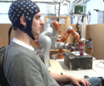 A person wearing an EEG cap and controlling a robotic arm using brain signals.