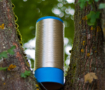 A cylindrical spool or reel with blue ends that is attached between two tree trunks.